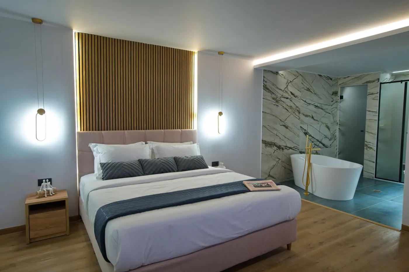 A suite with a wooden headboard and a bath behind glass