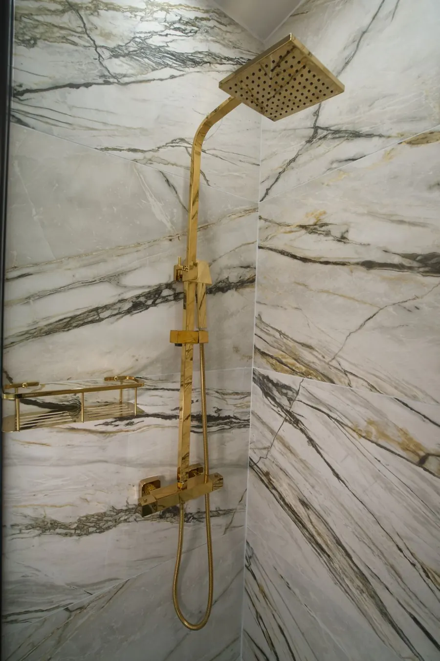 A gold rain shower in a marble shower room